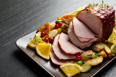 Photo of Tasty baked ham served with vegetables and oranges on black table