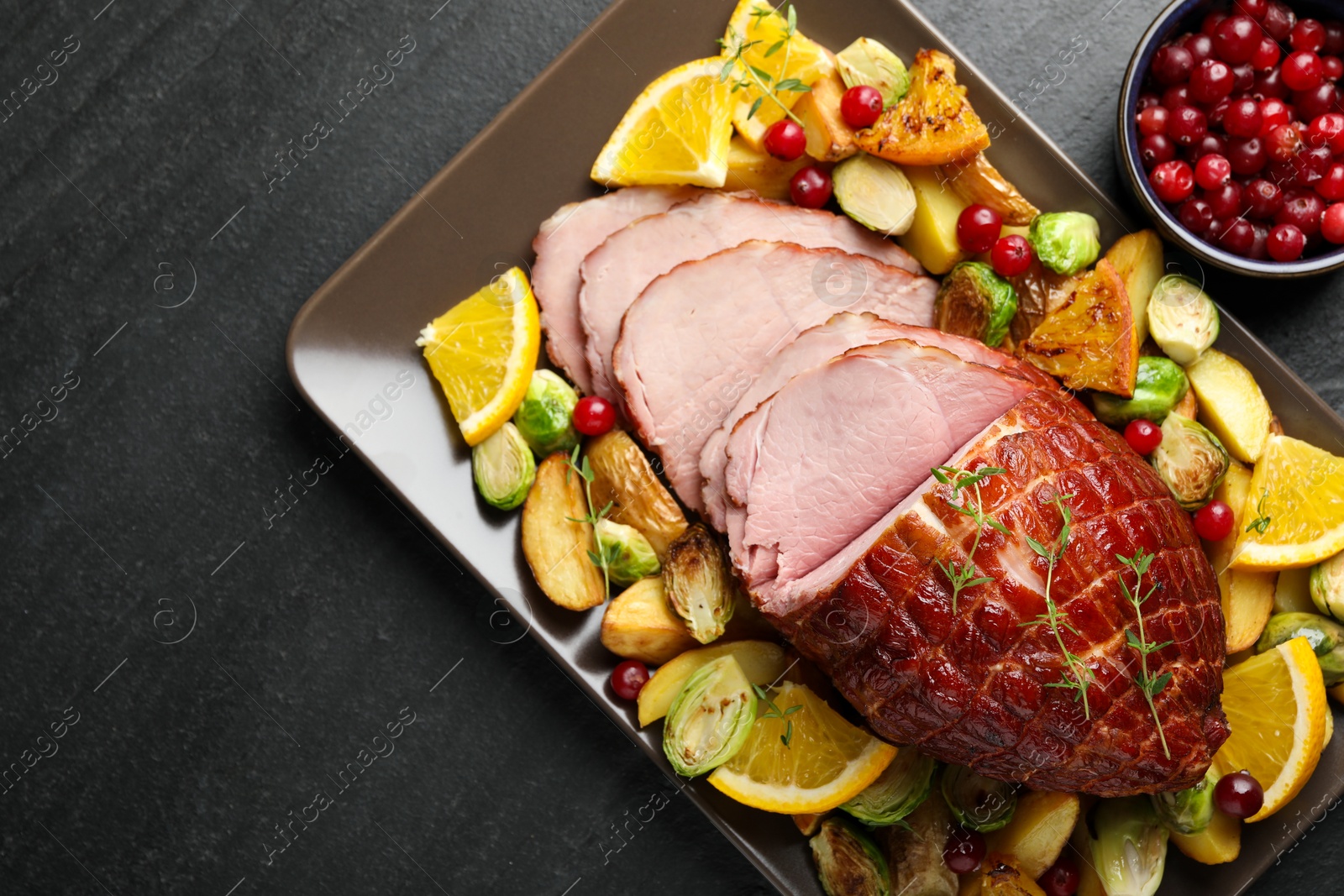 Photo of Tasty baked ham served with vegetables and oranges on black table, top view