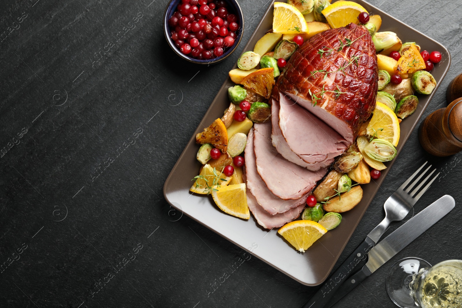 Photo of Tasty baked ham served with vegetables and oranges on black table, flat lay. Space for text