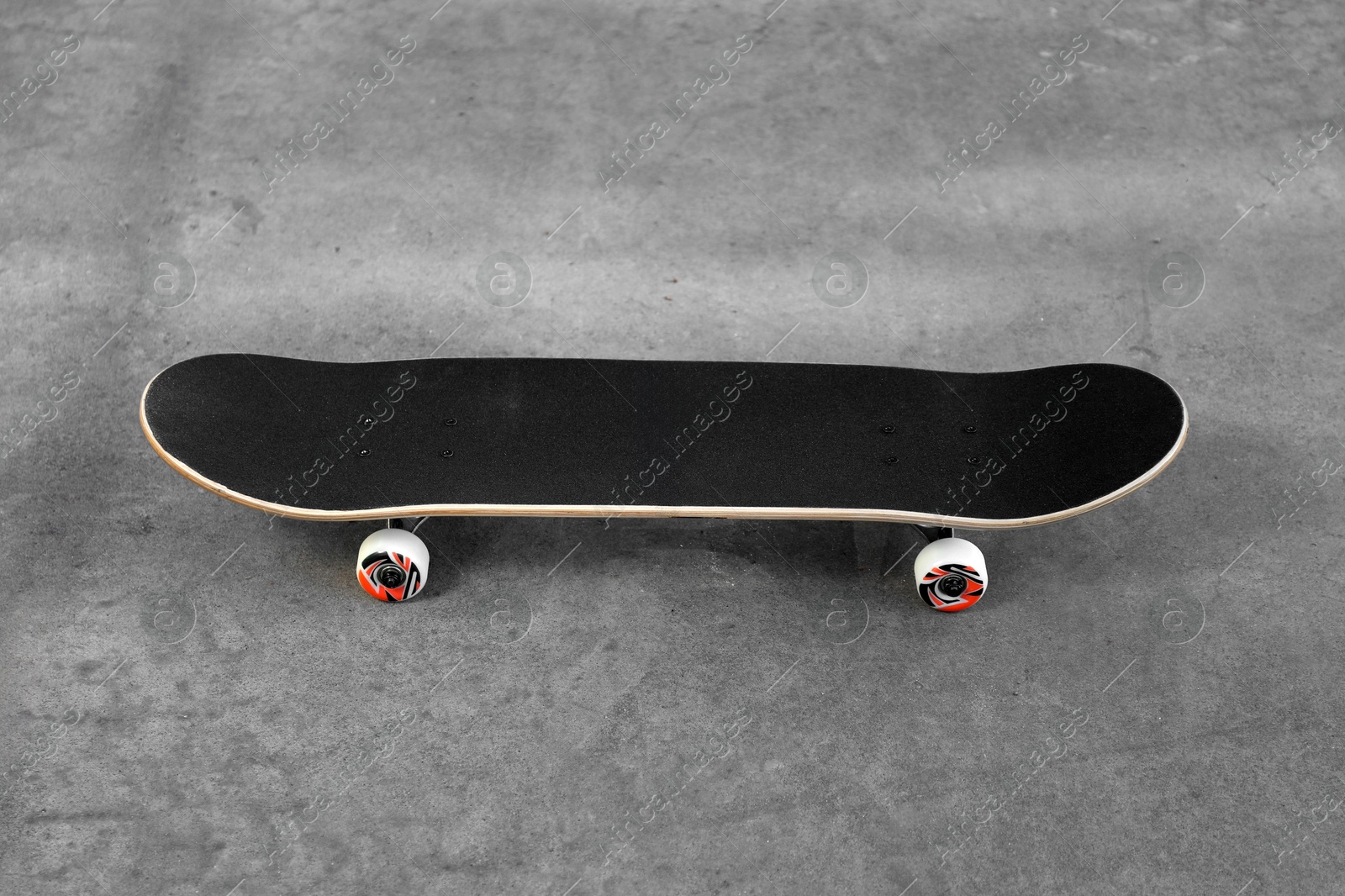 Photo of One modern skateboard with black griptape on ground outdoors