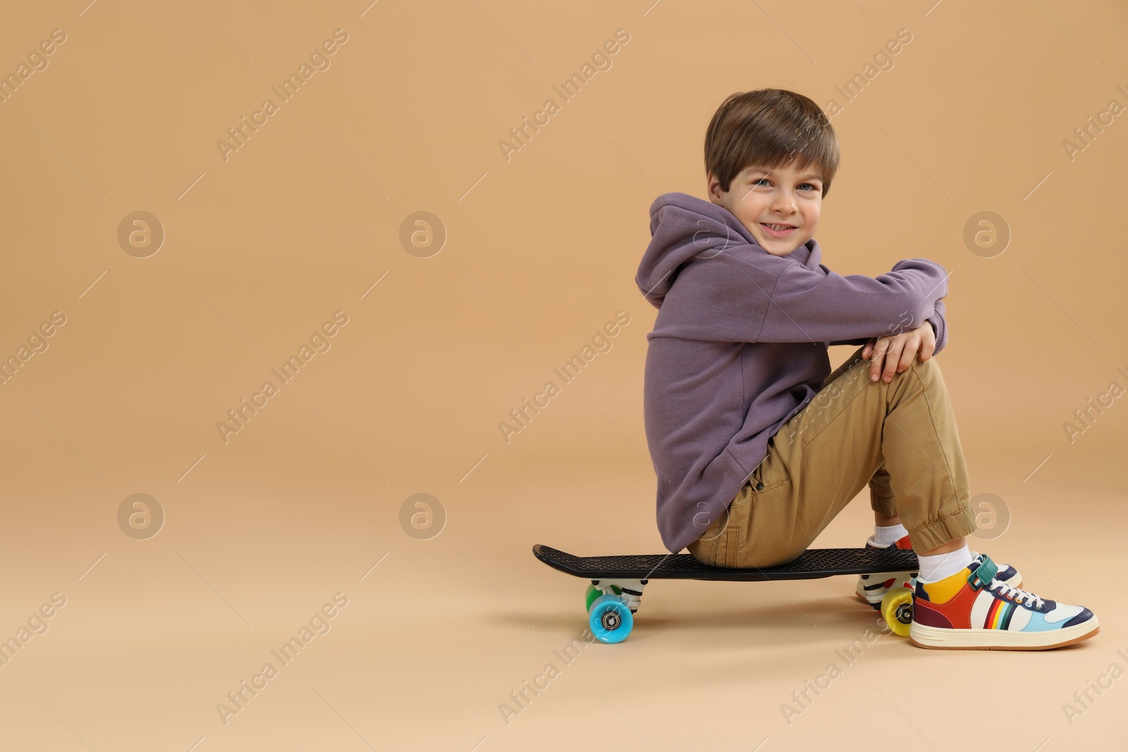 Photo of Little boy with skateboard on beige background, space for text