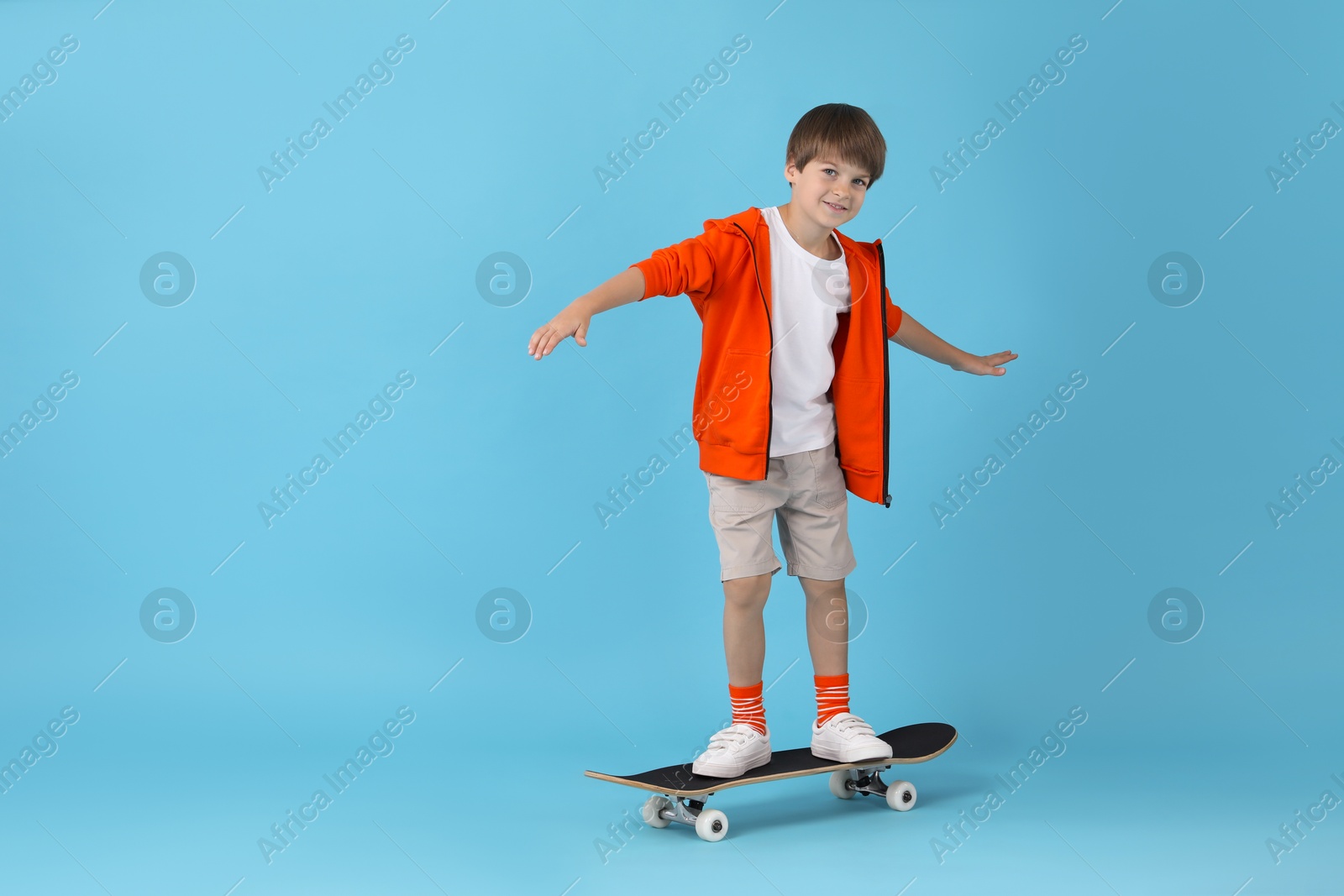 Photo of Little boy with skateboard on light blue background, space for text