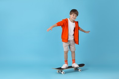 Photo of Little boy with skateboard on light blue background, space for text