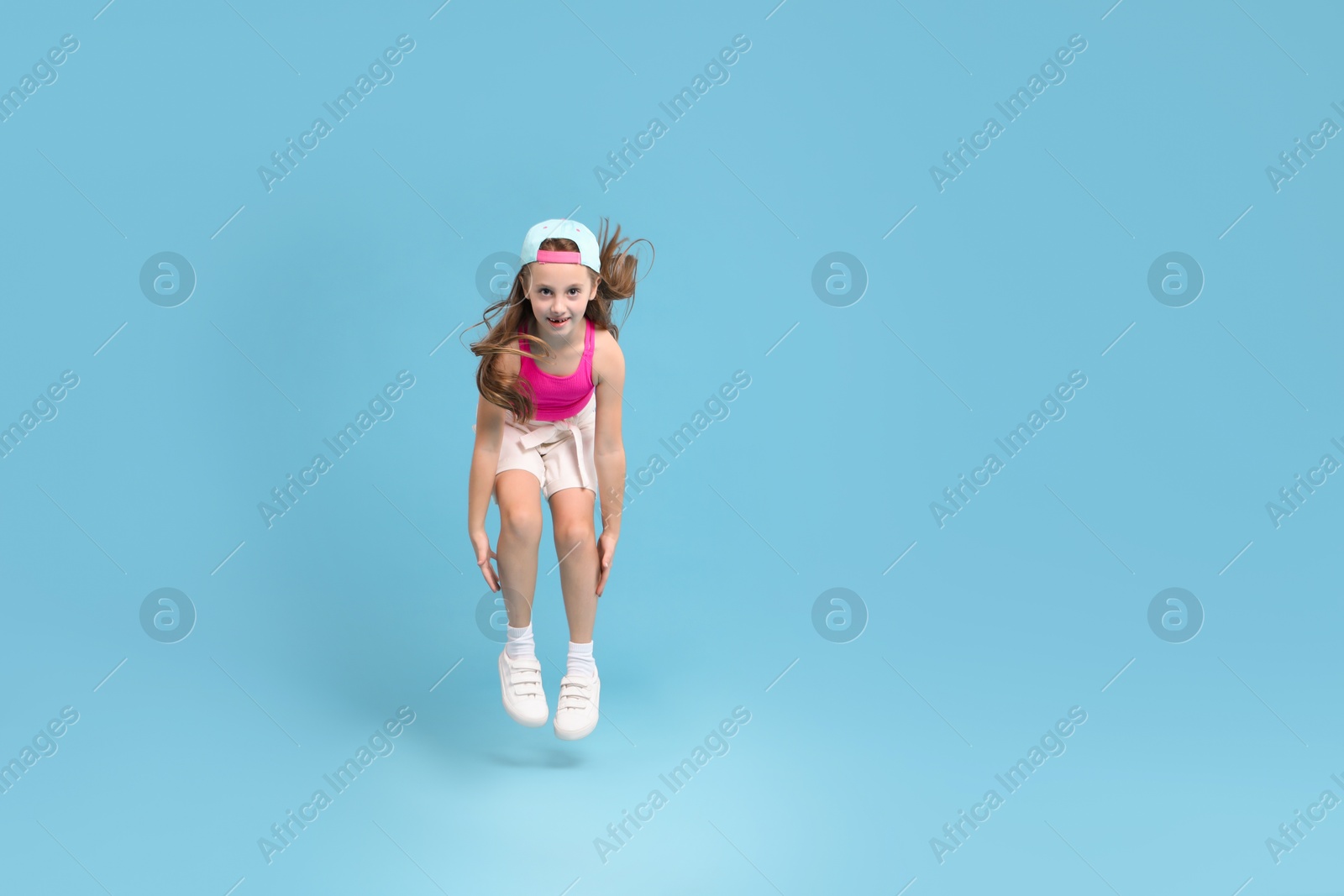 Photo of Cute little girl jumping on light blue background