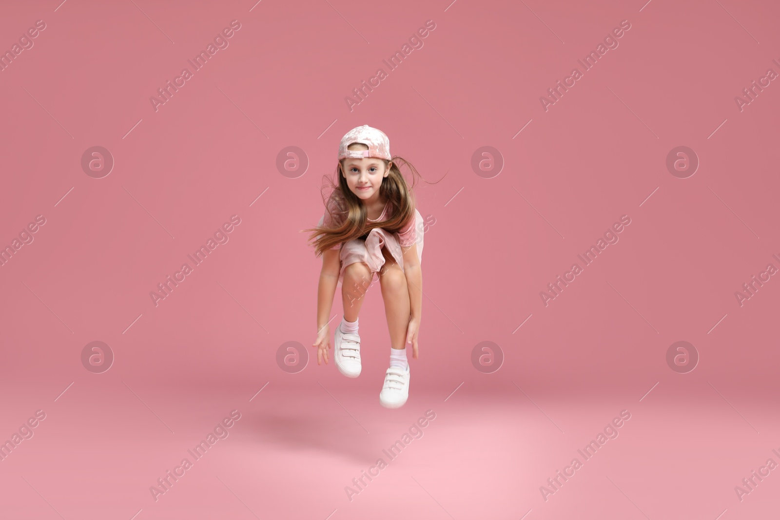 Photo of Cute little girl jumping on pink background