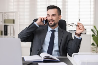 Photo of Happy banker talking on smartphone at table in office