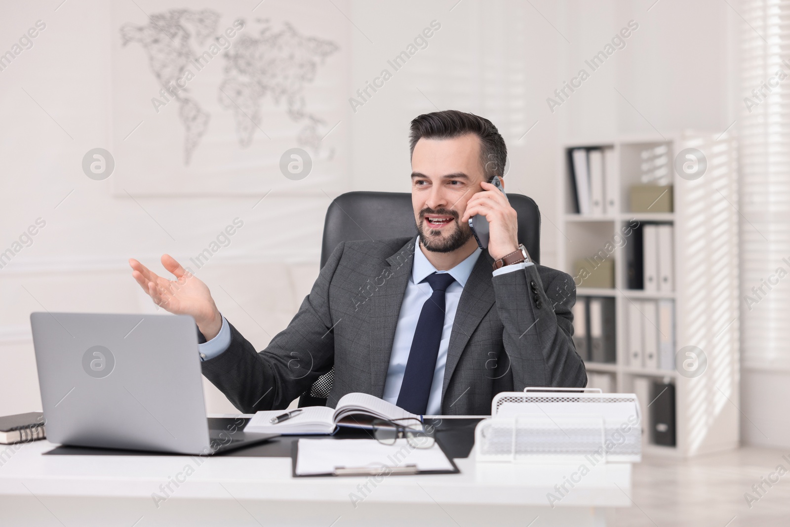 Photo of Happy banker talking on smartphone at table in office