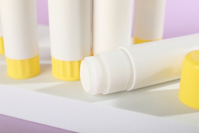 Photo of Many glue sticks on violet background, closeup