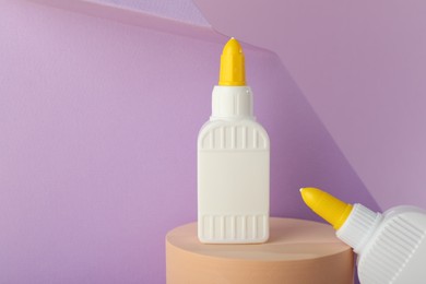 Photo of Bottles of glue and wooden podium on violet background, space for text