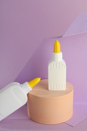 Photo of Bottles of glue and wooden podium on violet background