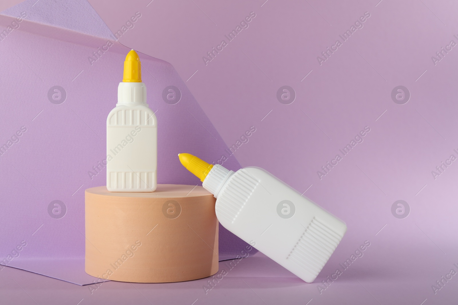 Photo of Bottles of glue and wooden podium on violet background