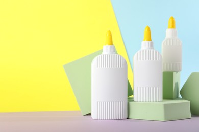 Photo of Bottles of glue and podiums on table against color background