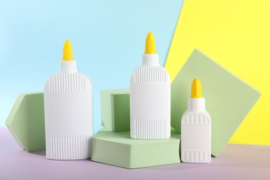 Photo of Bottles of glue and podiums on table against color background