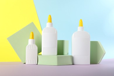 Photo of Bottles of glue and podiums on table against color background