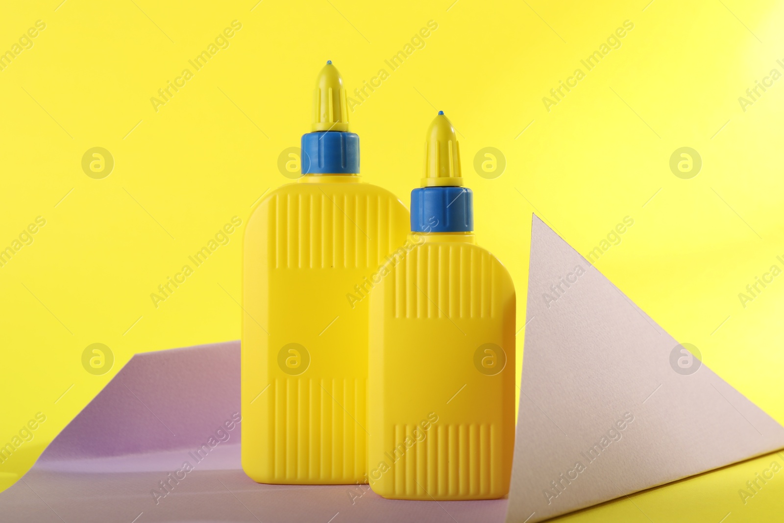 Photo of Bottles of glue and violet paper sheet on yellow background