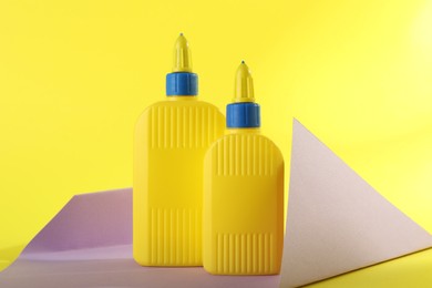 Photo of Bottles of glue and violet paper sheet on yellow background