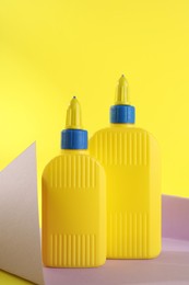 Photo of Bottles of glue and violet paper sheet on yellow background