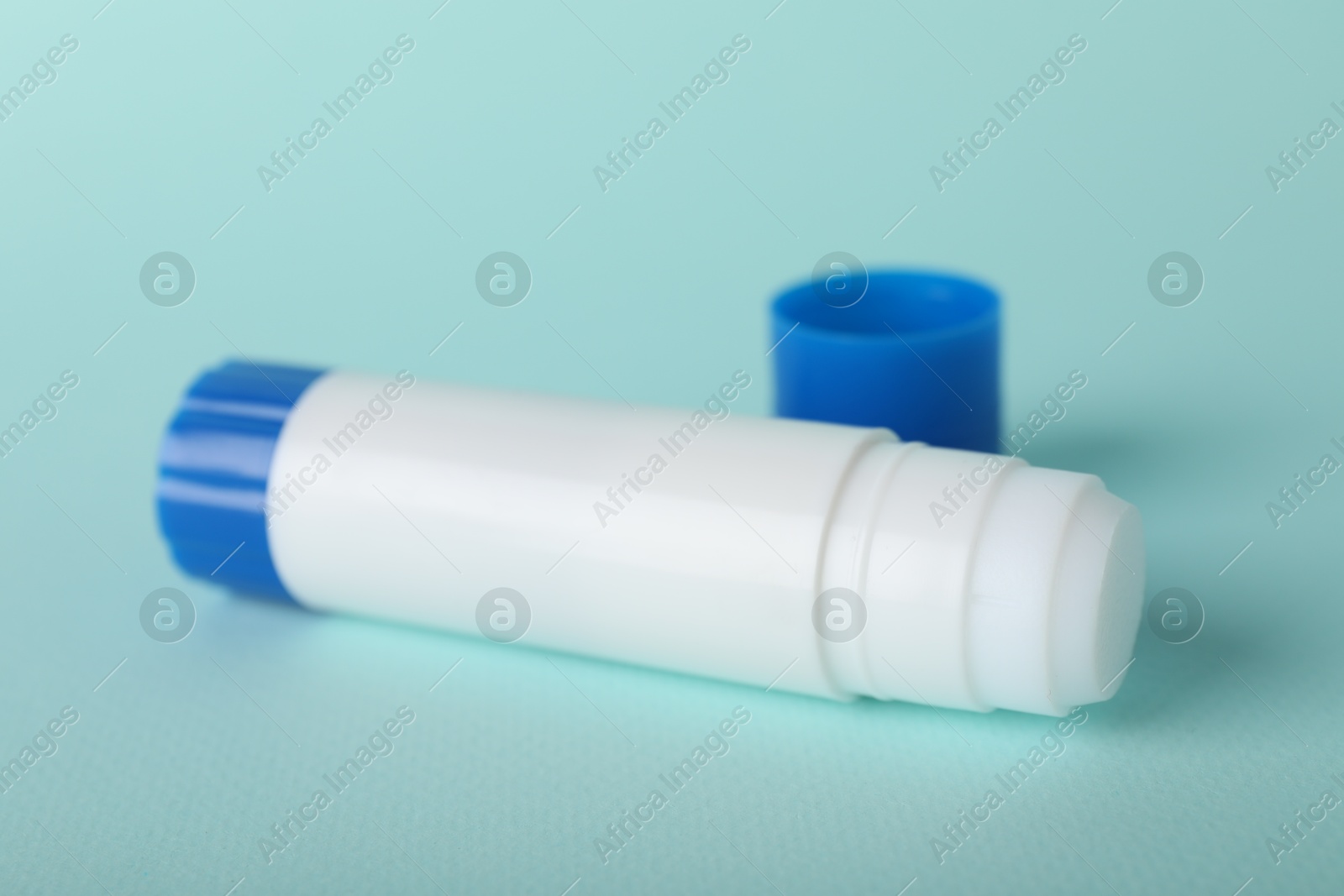 Photo of Glue stick and cap on light blue background, closeup