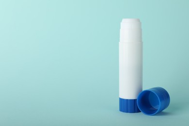 Photo of Glue stick and cap on light blue background, space for text