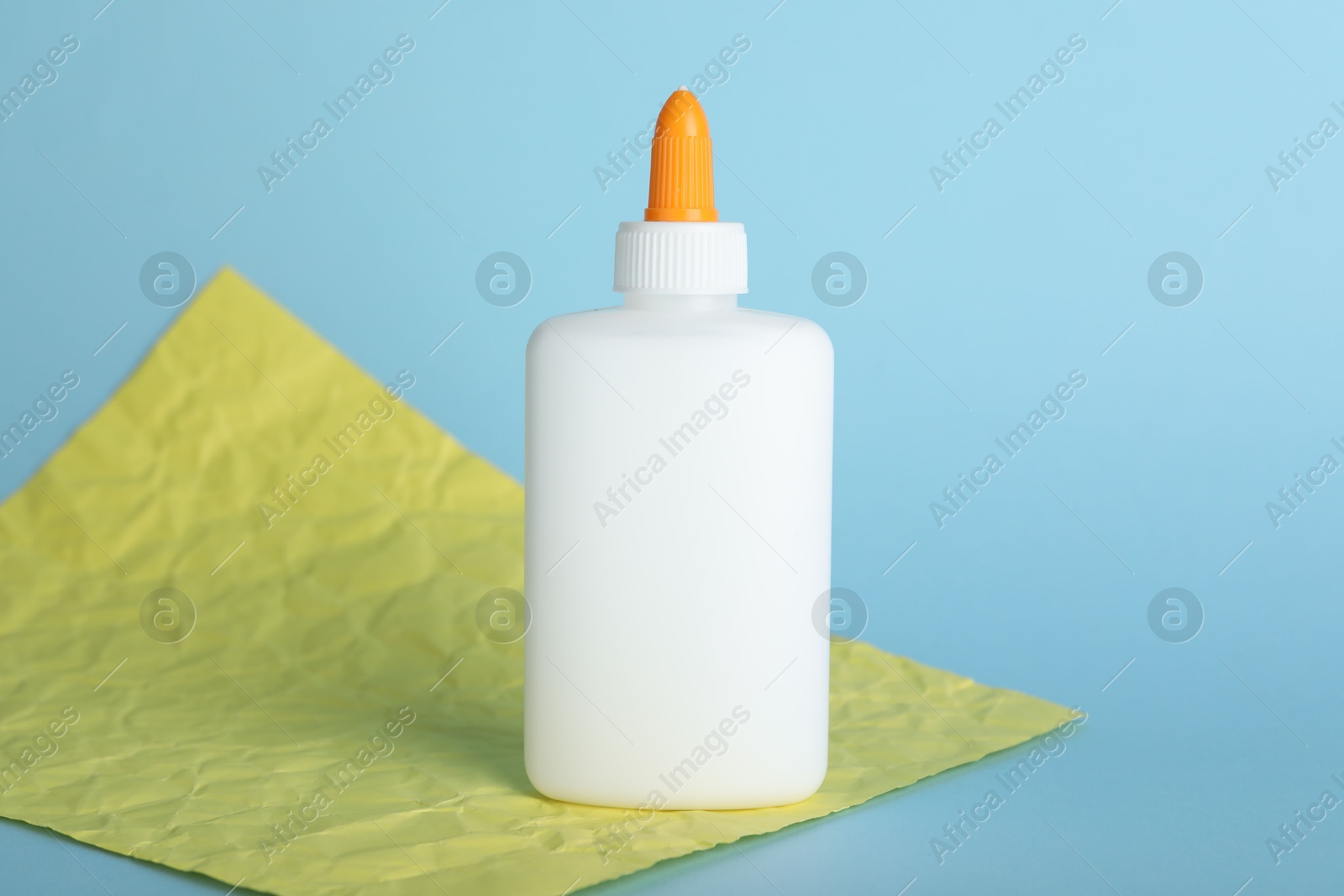 Photo of Bottle of glue and yellow paper sheet on light blue background