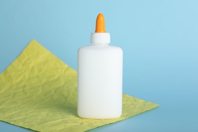 Photo of Bottle of glue and yellow paper sheet on light blue background