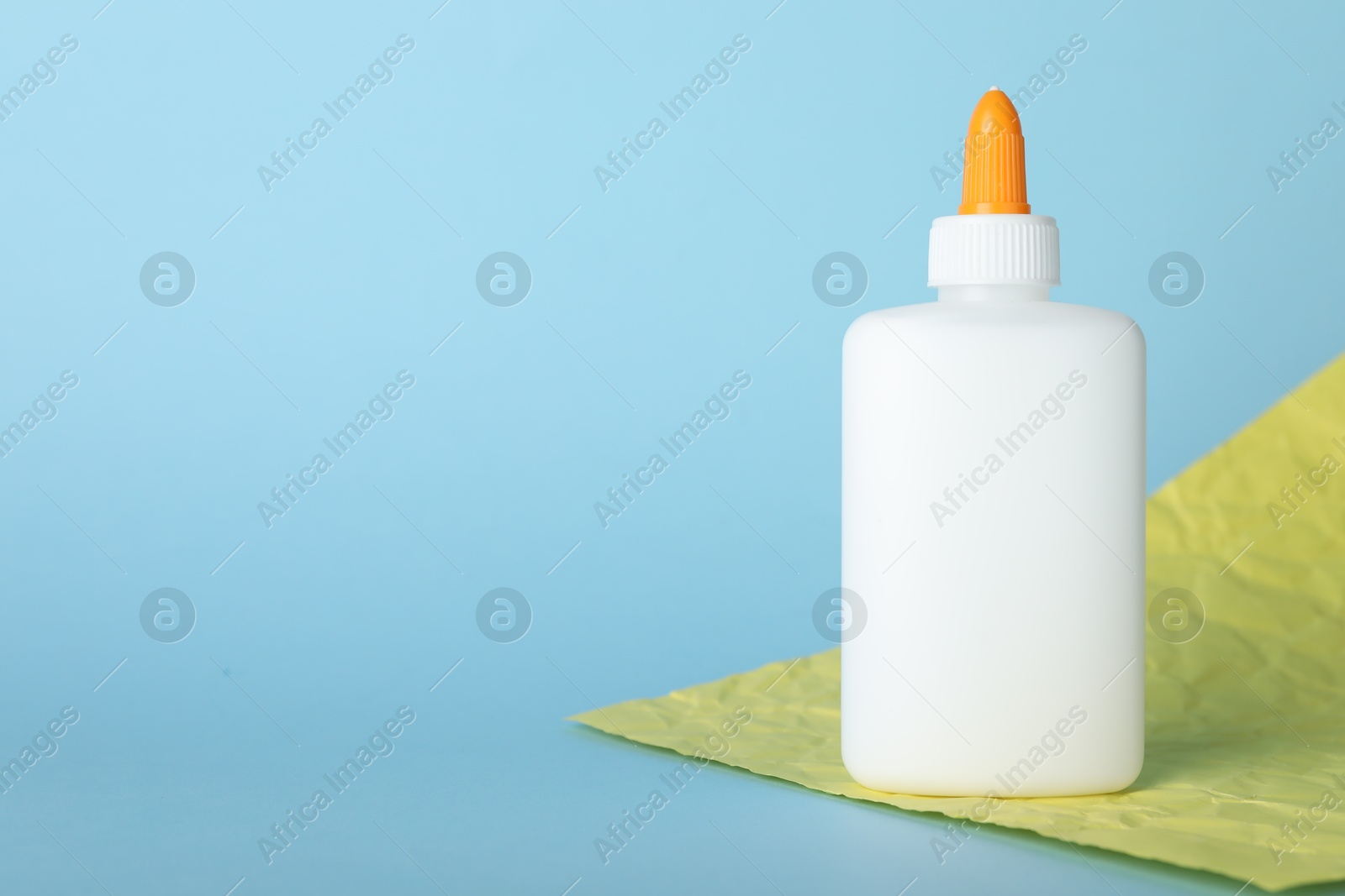 Photo of Bottle of glue and yellow paper sheet on light blue background, space for text