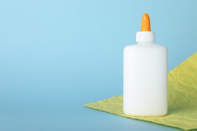 Photo of Bottle of glue and yellow paper sheet on light blue background, space for text