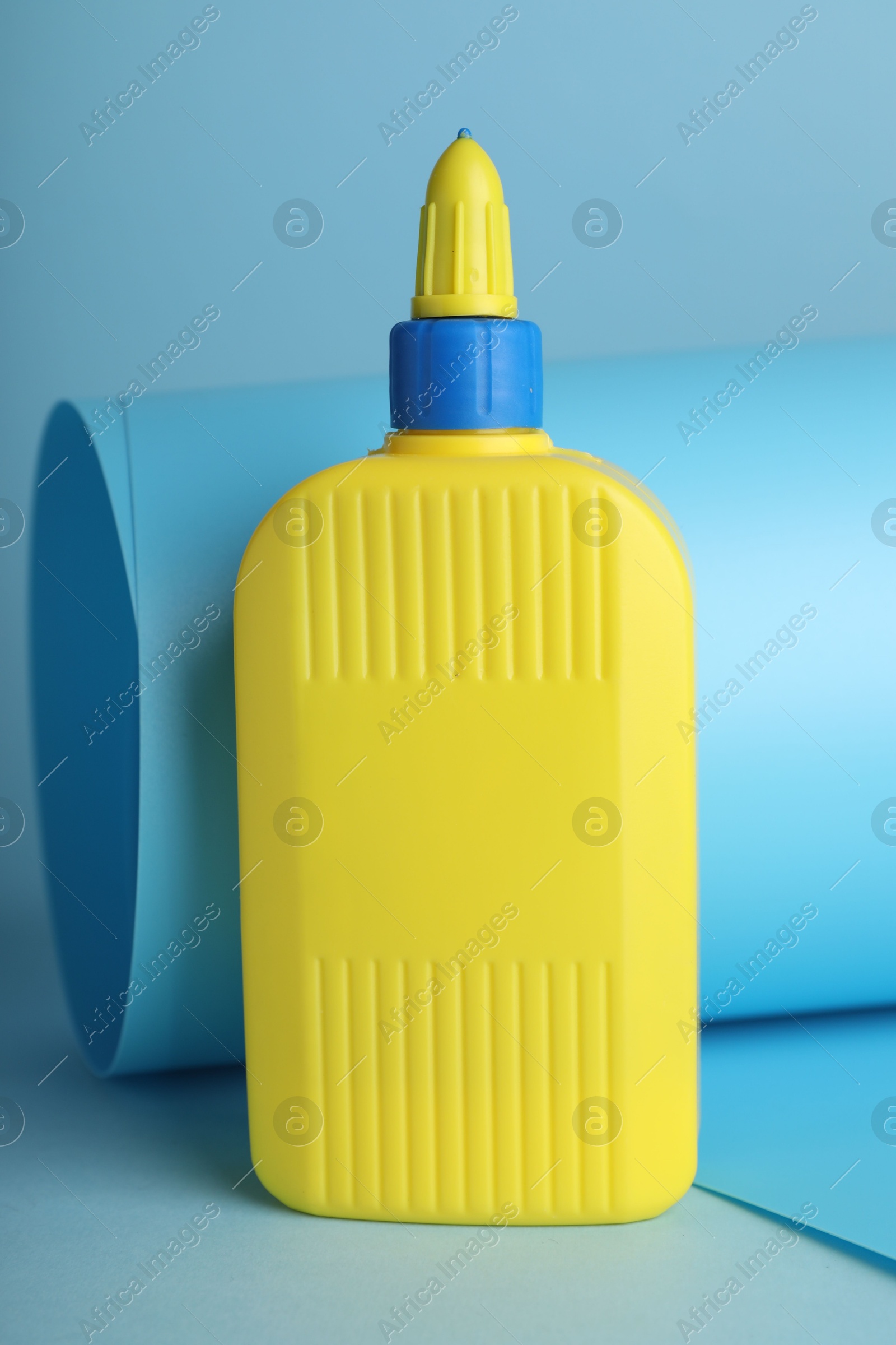 Photo of Bottle of glue and color paper sheet on light blue background, closeup