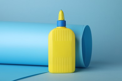 Photo of Bottle of glue and color paper sheet on light blue background, closeup