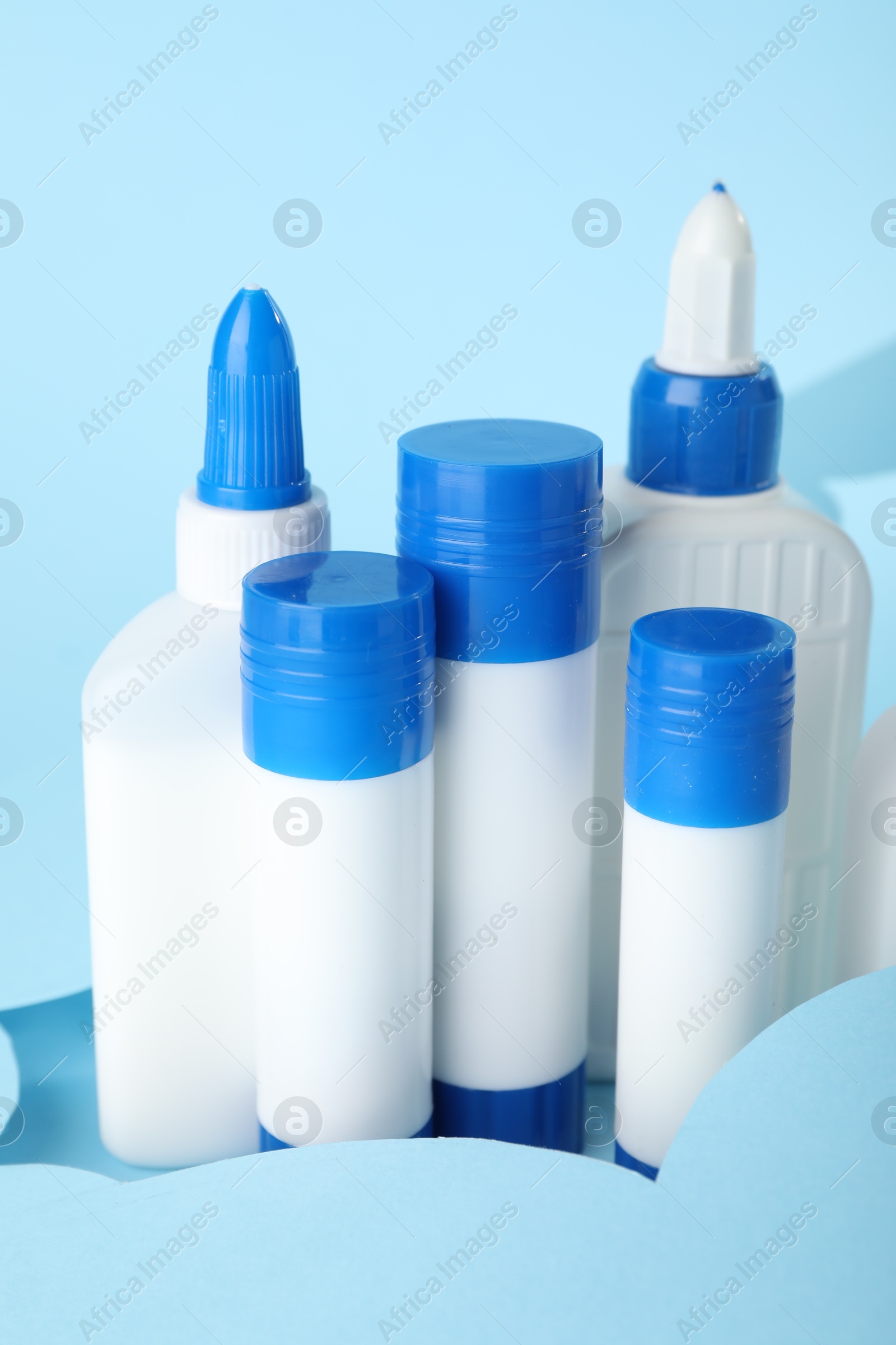 Photo of Different types of glue and paper cutout on light blue background, closeup