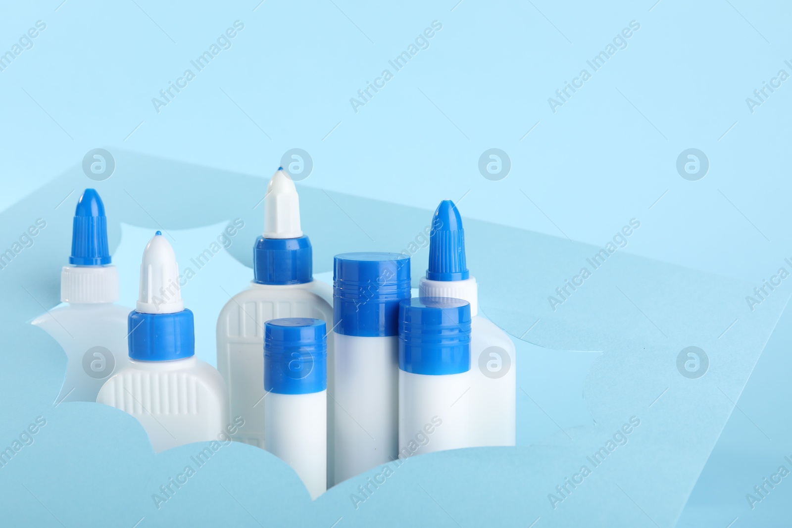 Photo of Different types of glue and paper cutout on light blue background, closeup