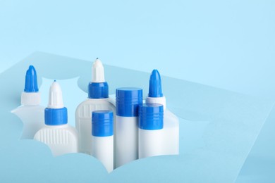 Photo of Different types of glue and paper cutout on light blue background, closeup