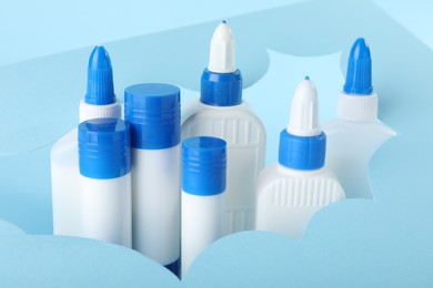 Photo of Different types of glue and paper cutout on light blue background, closeup