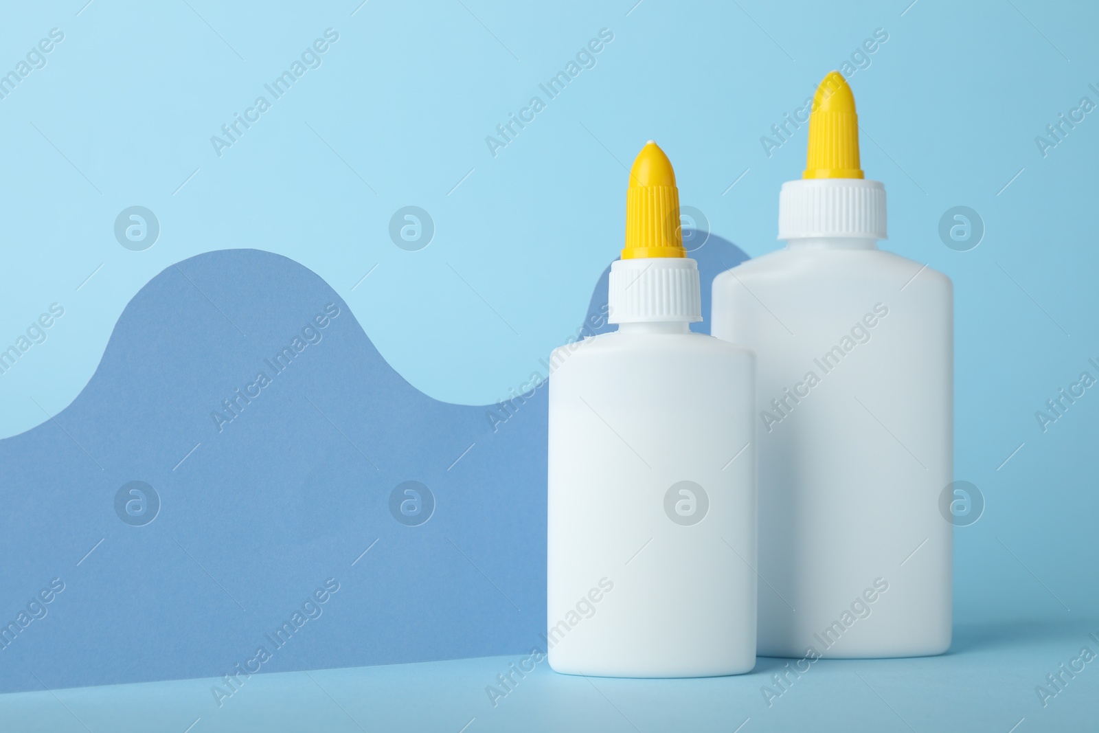 Photo of Bottles of glue and paper cutout on light blue background