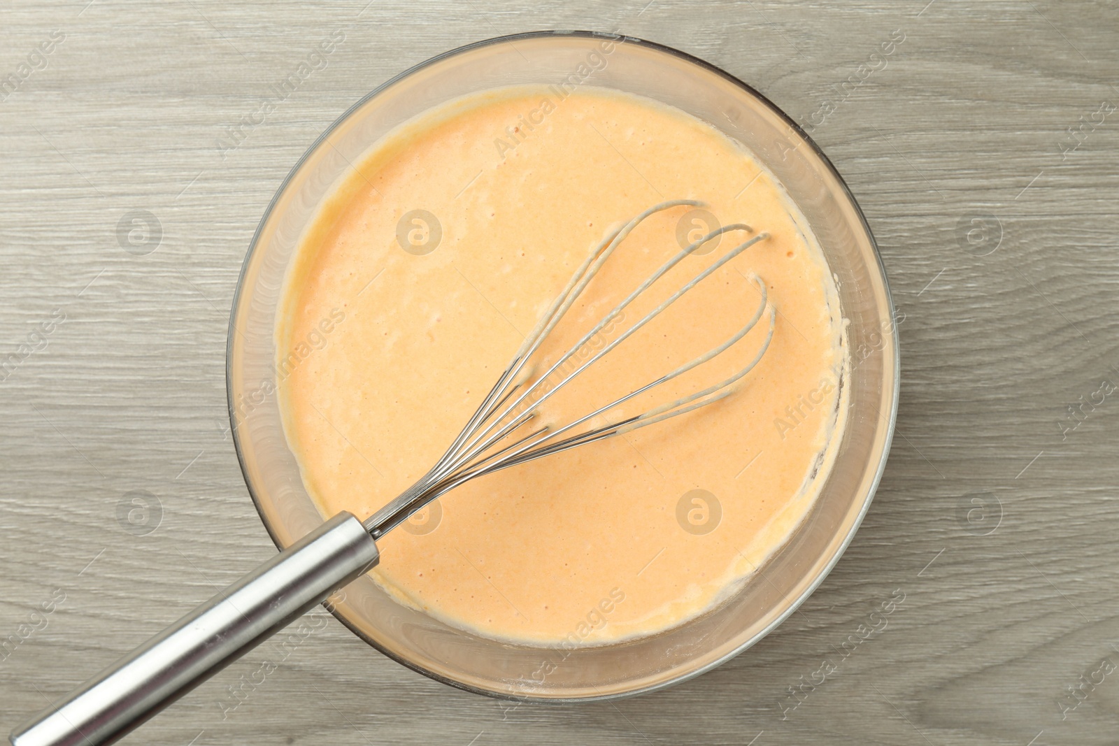 Photo of Bowl with dough for pumpkin pancakes and whisk on wooden table, top view