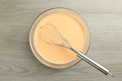 Photo of Bowl with dough for pumpkin pancakes and whisk on wooden table, top view