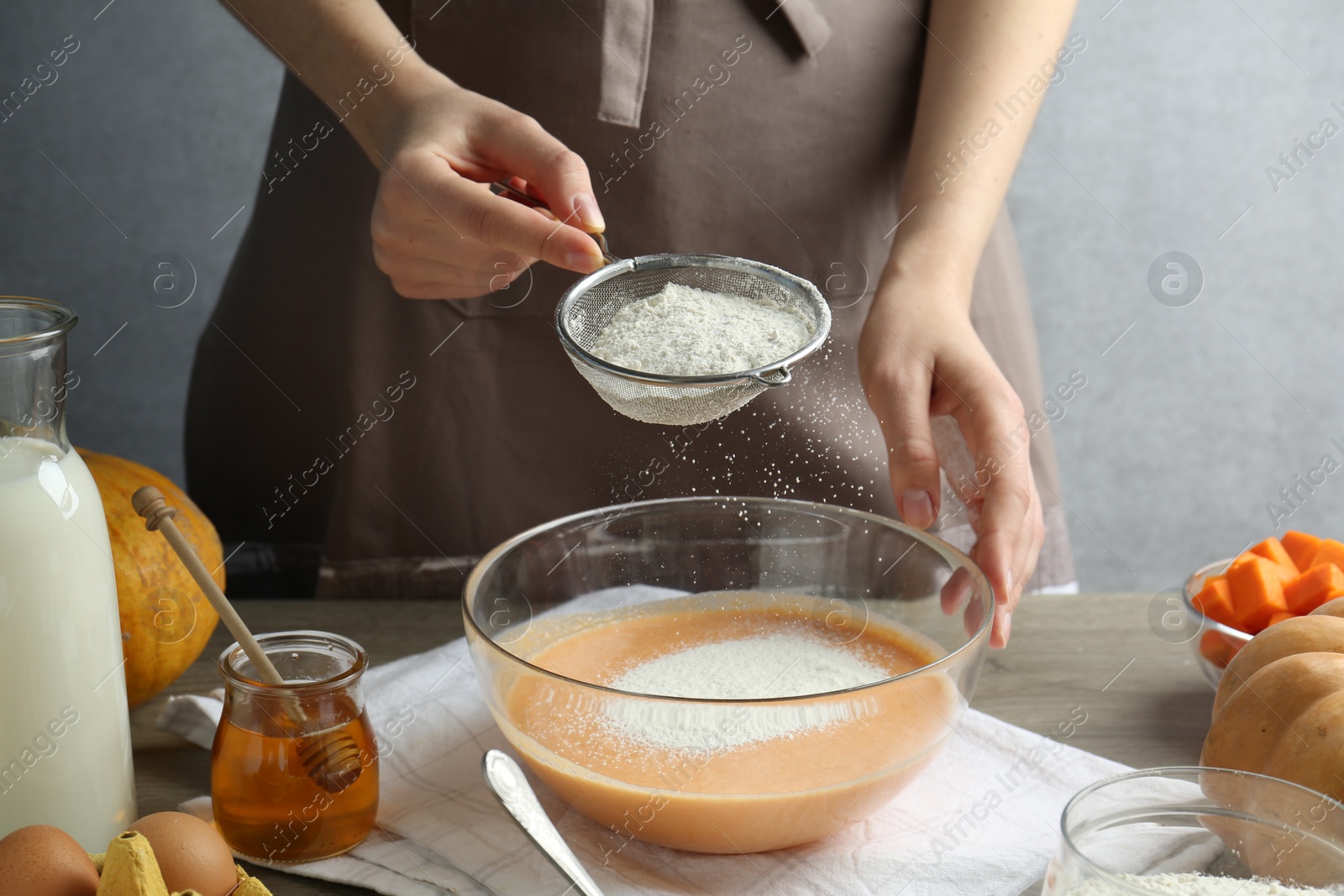 Photo of Making pumpkin pancakes. Woman adding flour to dough at table, closeup