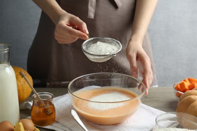 Photo of Making pumpkin pancakes. Woman adding flour to dough at table, closeup