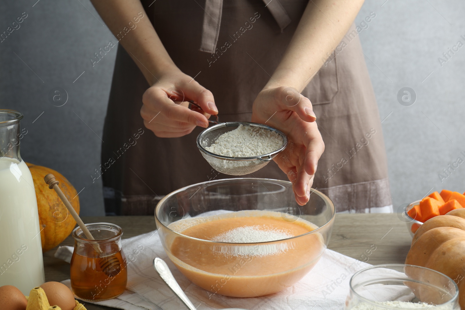 Photo of Making pumpkin pancakes. Woman adding flour to dough at table, closeup