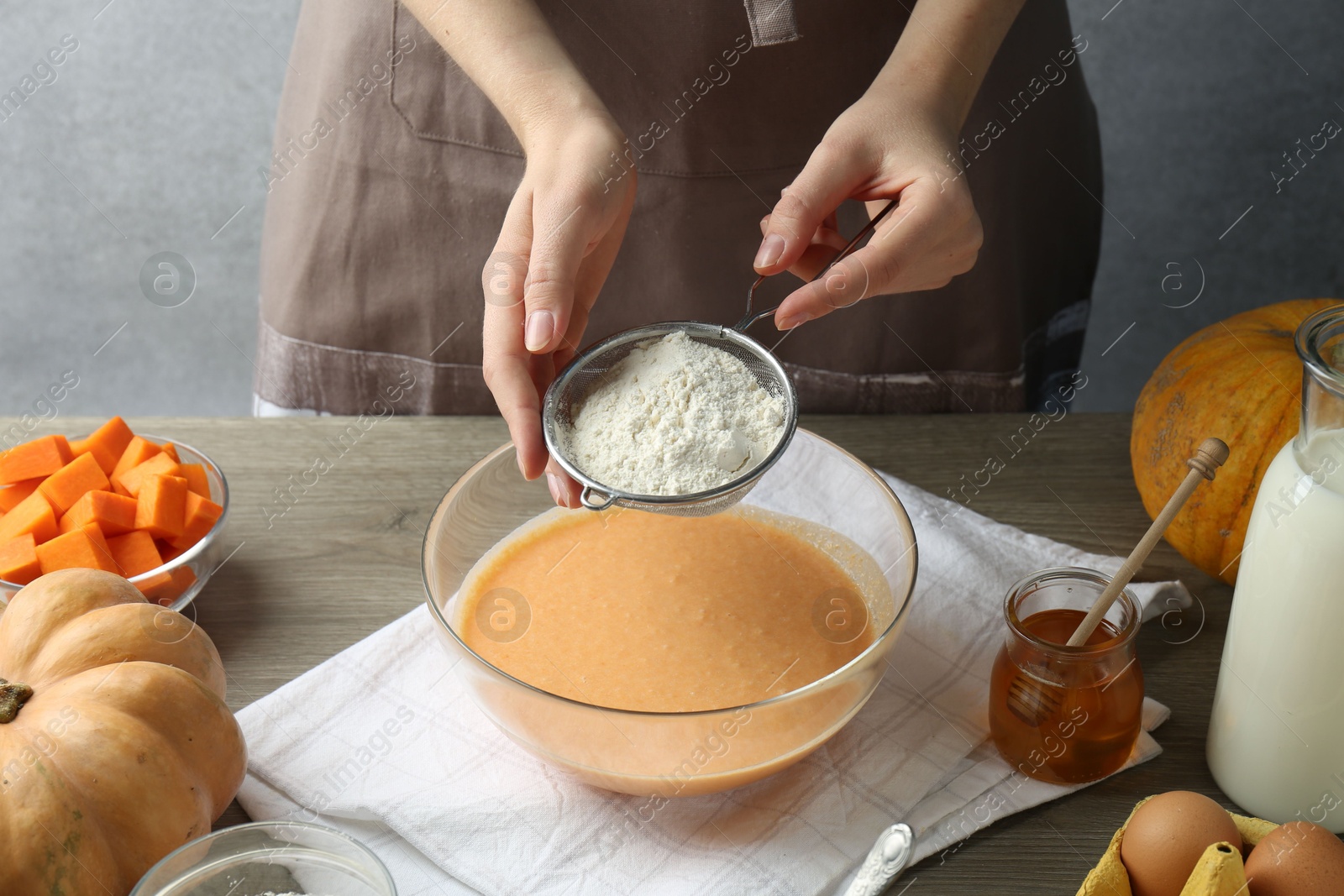 Photo of Making pumpkin pancakes. Woman adding flour to dough at table, closeup