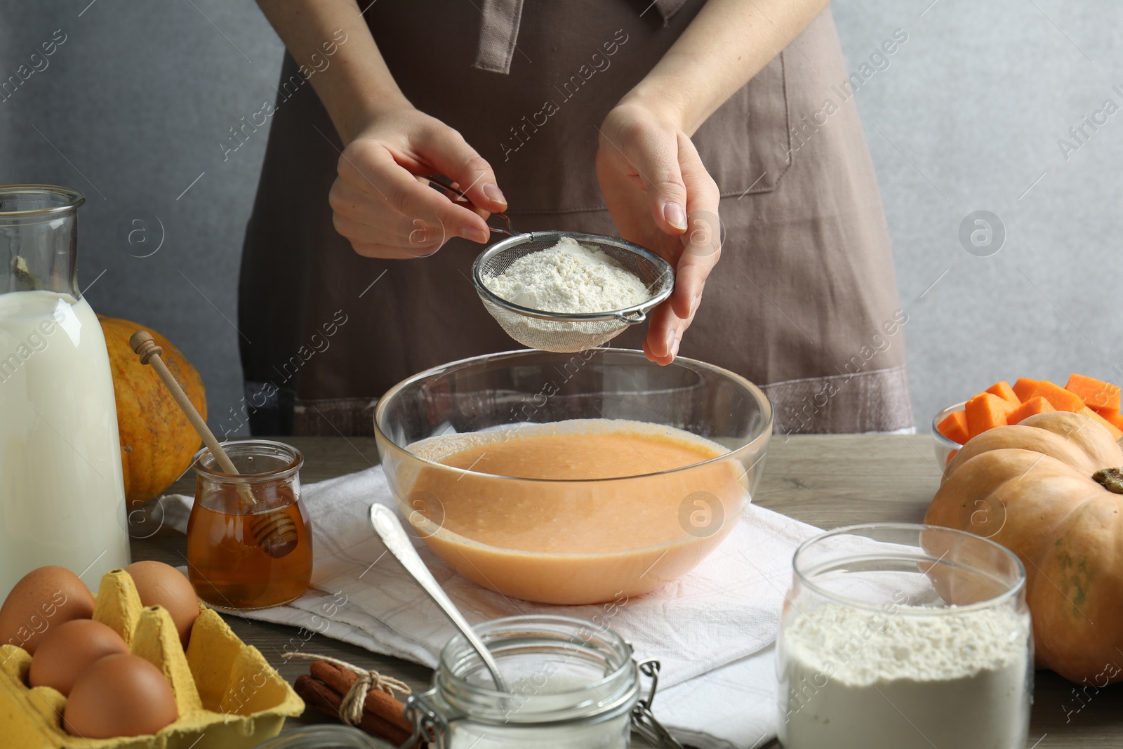 Photo of Making pumpkin pancakes. Woman adding flour to dough at table, closeup