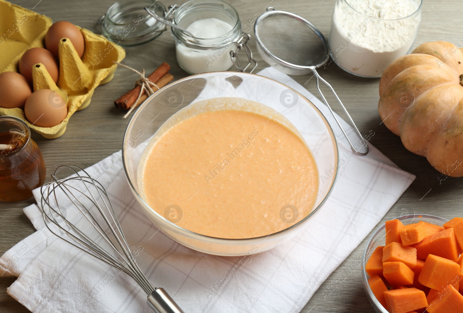 Photo of Bowl with dough and ingredients for pumpkin pancakes on wooden table