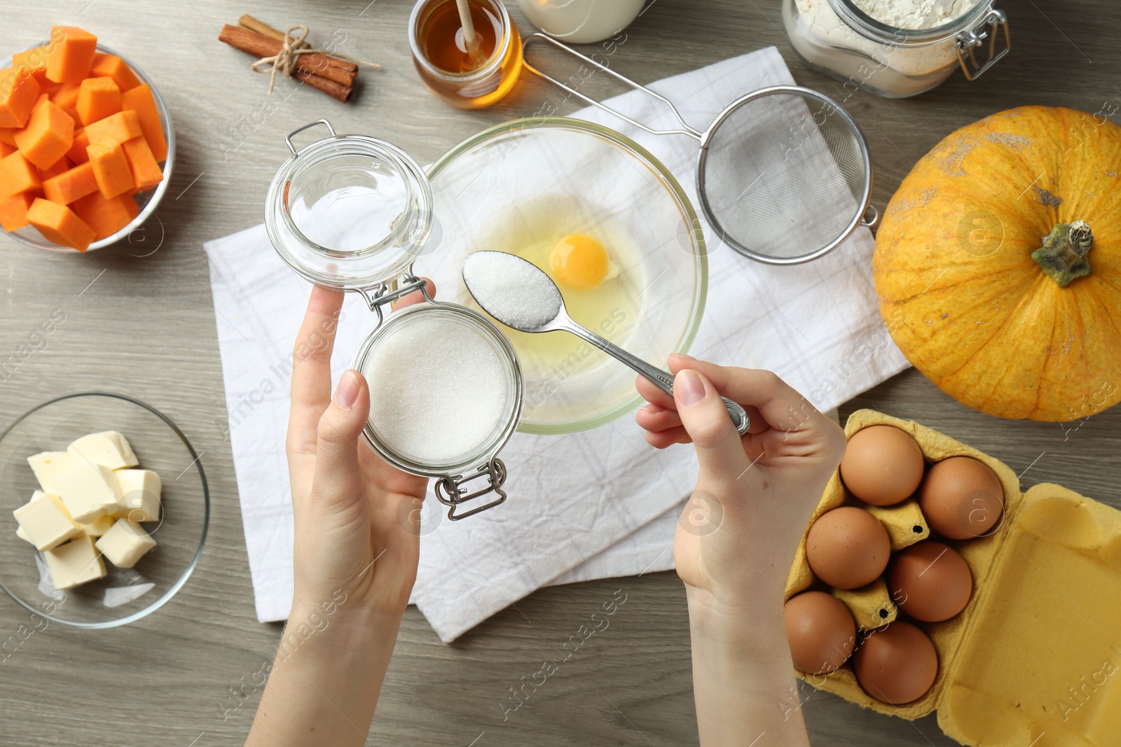 Photo of Making pumpkin pancakes. Woman adding sugar to eggs at wooden table, top view