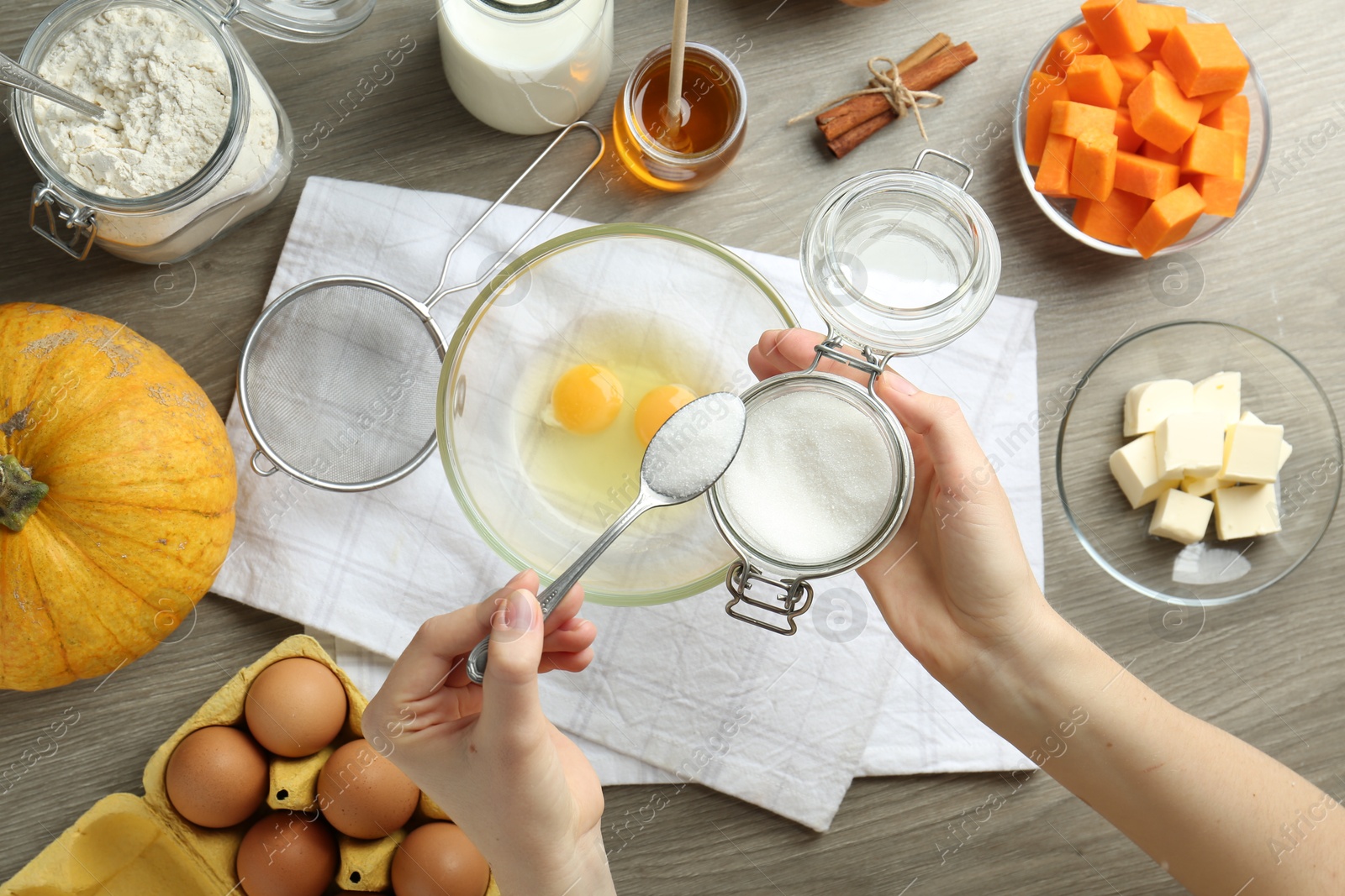 Photo of Making pumpkin pancakes. Woman adding sugar to eggs at wooden table, top view