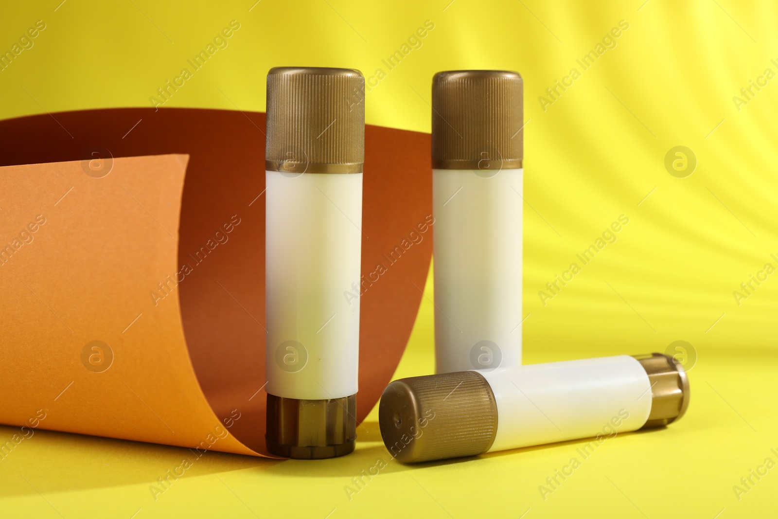 Photo of Sticks of glue on yellow background. School stationery