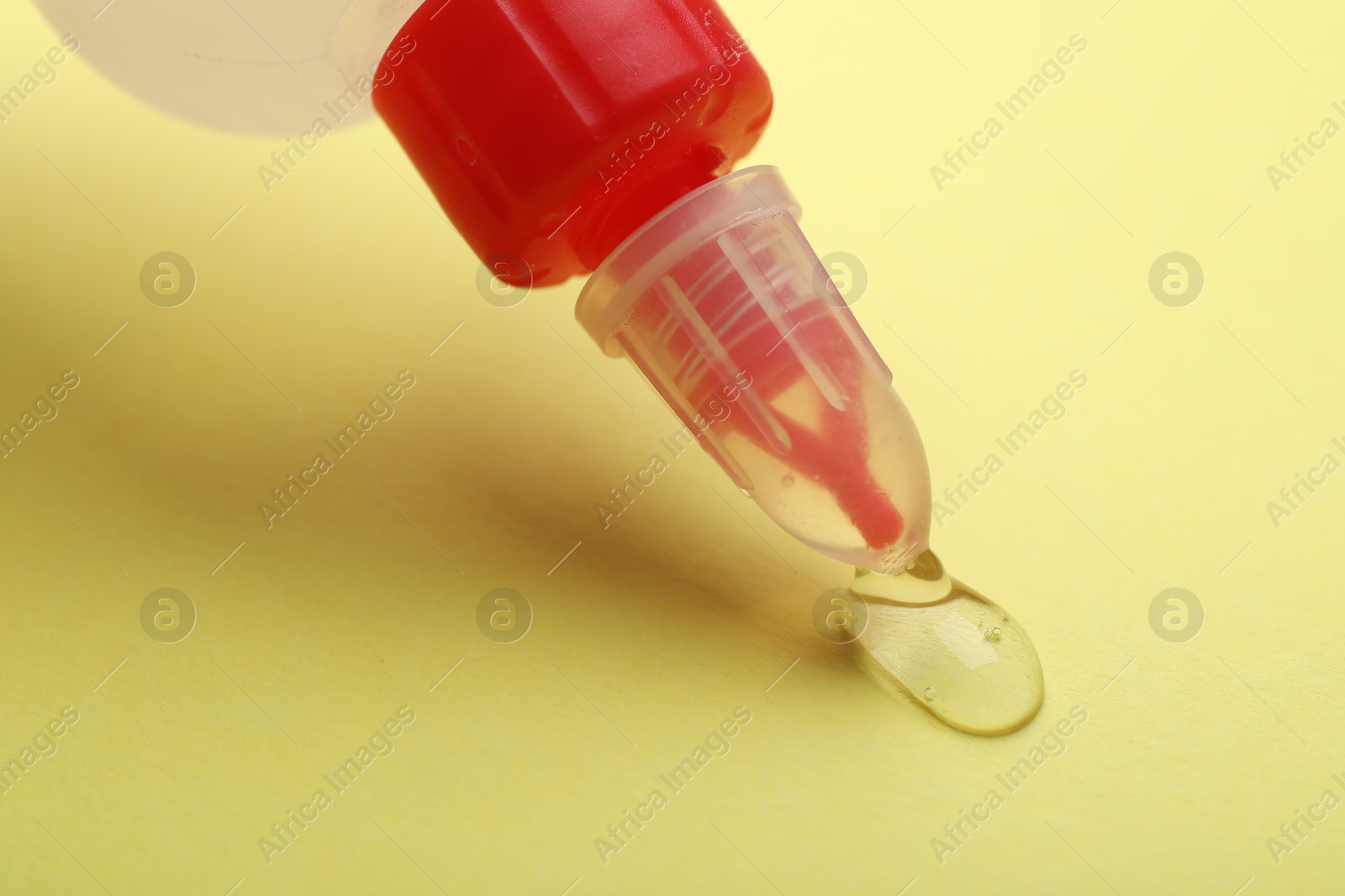 Photo of Applying glue from bottle on yellow background, closeup