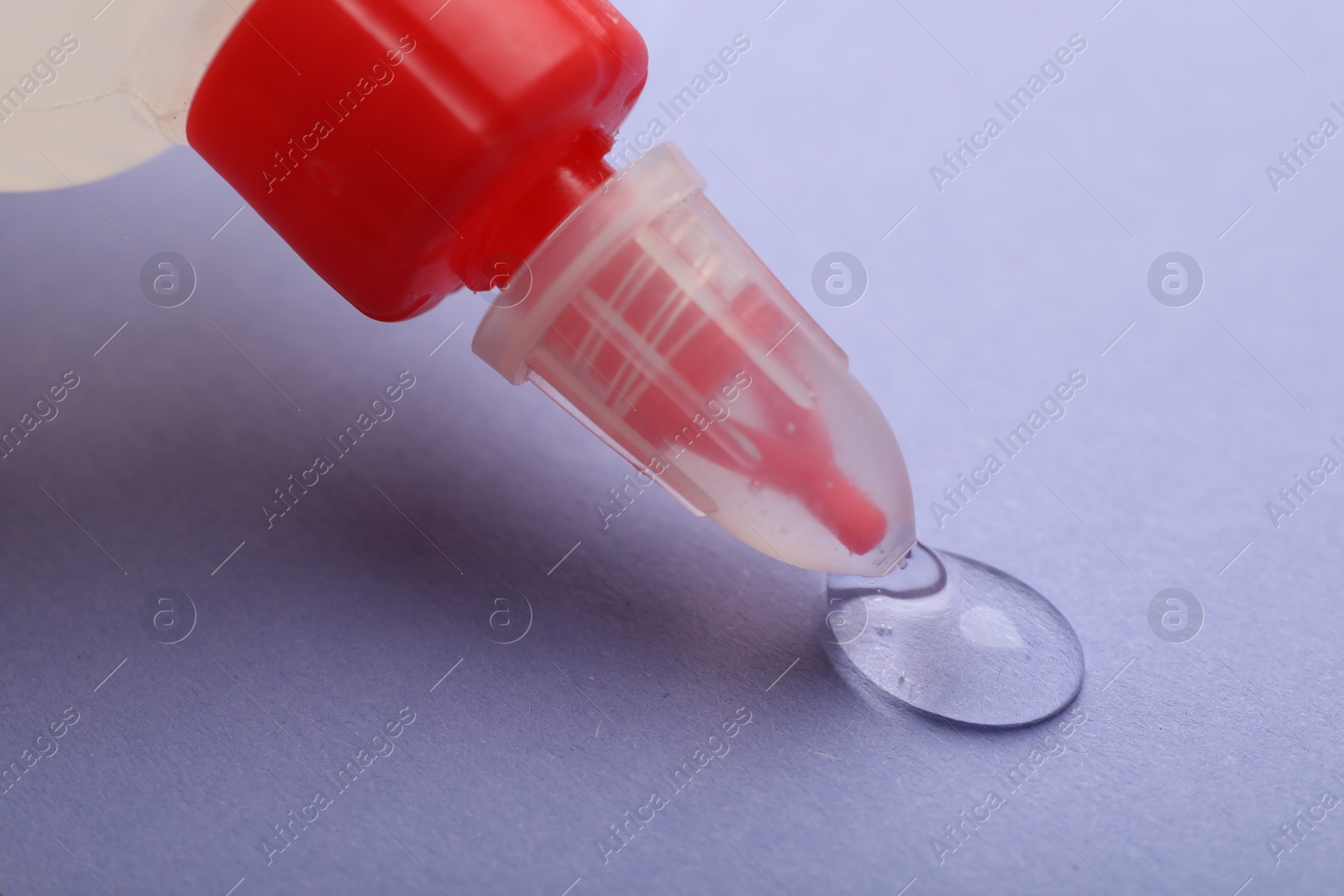 Photo of Applying glue from bottle on violet background, closeup