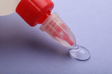 Photo of Applying glue from bottle on violet background, closeup