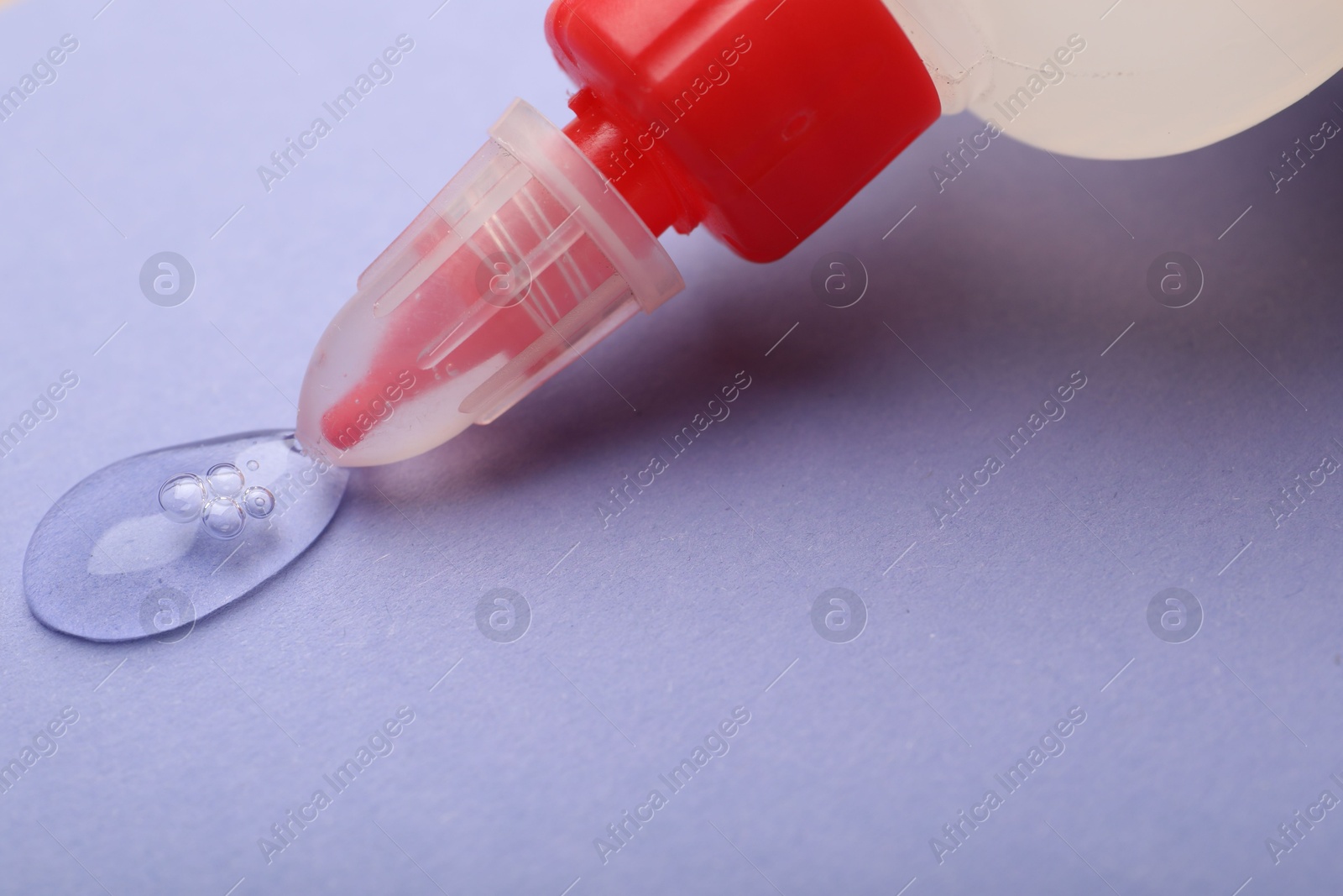 Photo of Applying glue from bottle on violet background, closeup