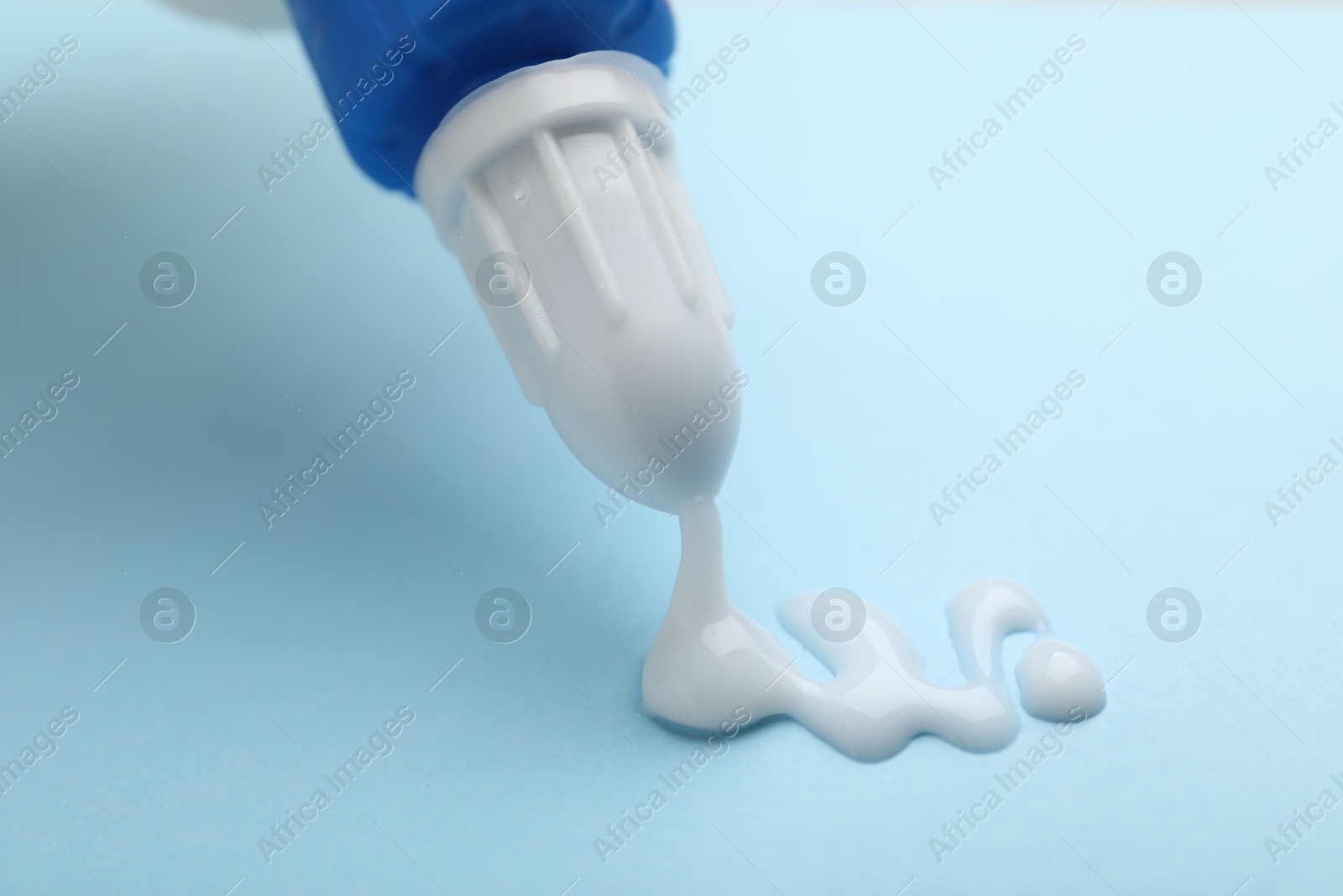 Photo of Applying glue from bottle on light blue background, closeup